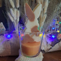 Bougie artisanale représentant un petit lapin bicolore avec un cœur sculpté, disponible en format pot de 265g ou palet de 80g, décoration de chambre et cadeau de naissance.