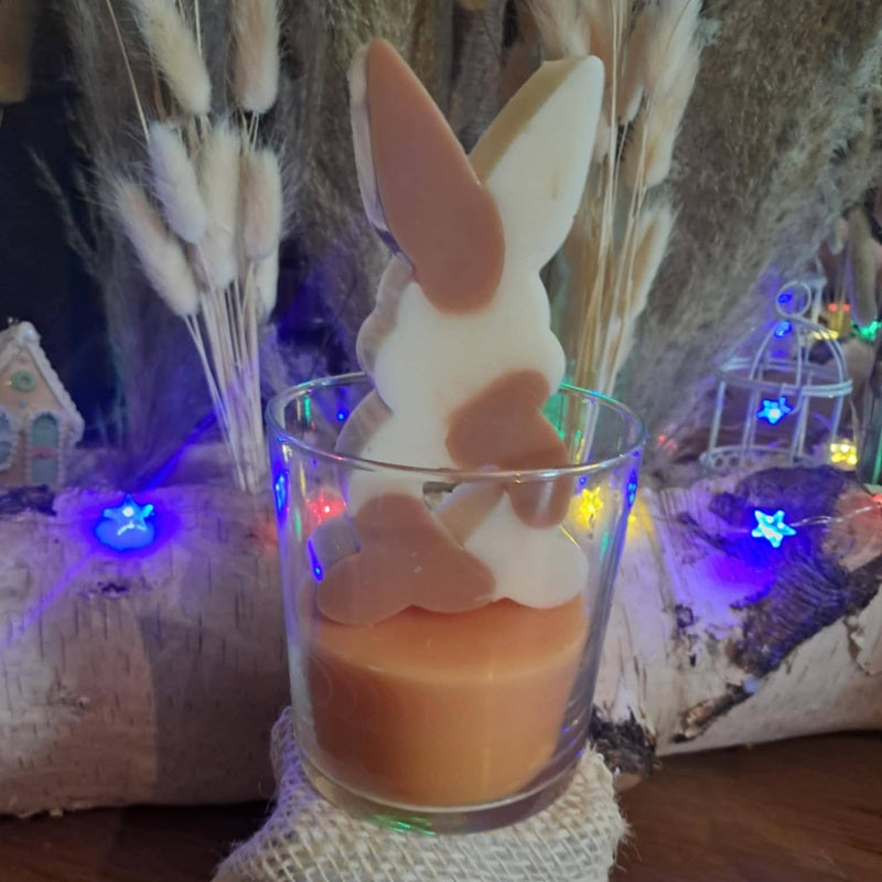 Bougie artisanale représentant un petit lapin bicolore avec un cœur sculpté, disponible en format pot de 265g ou palet de 80g, décoration de chambre et cadeau de naissance.
