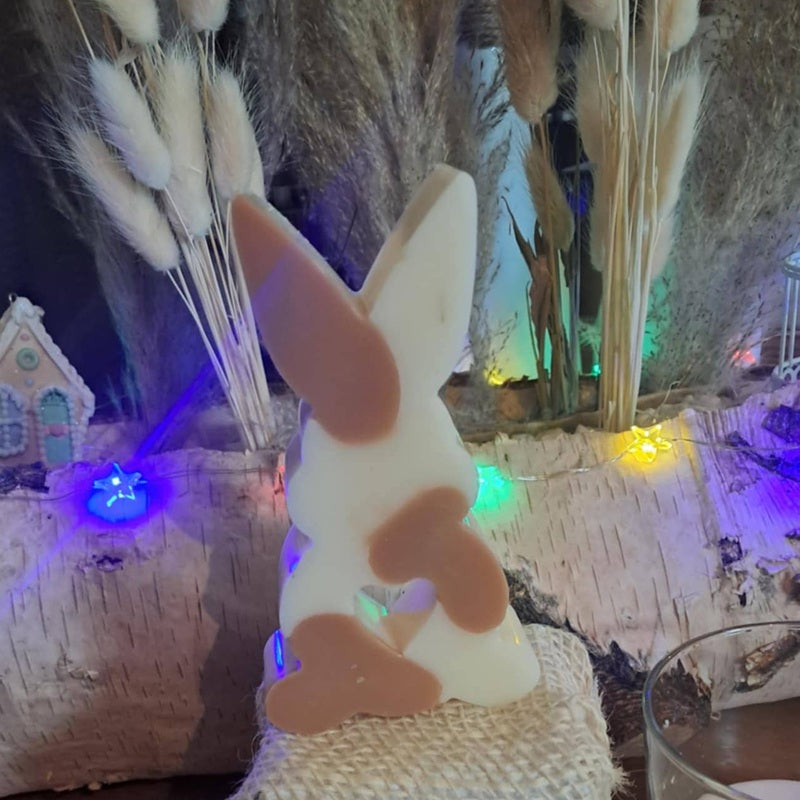 Bougie artisanale représentant un petit lapin bicolore avec un cœur sculpté, disponible en format pot de 265g ou palet de 80g, décoration de chambre et cadeau de naissance.