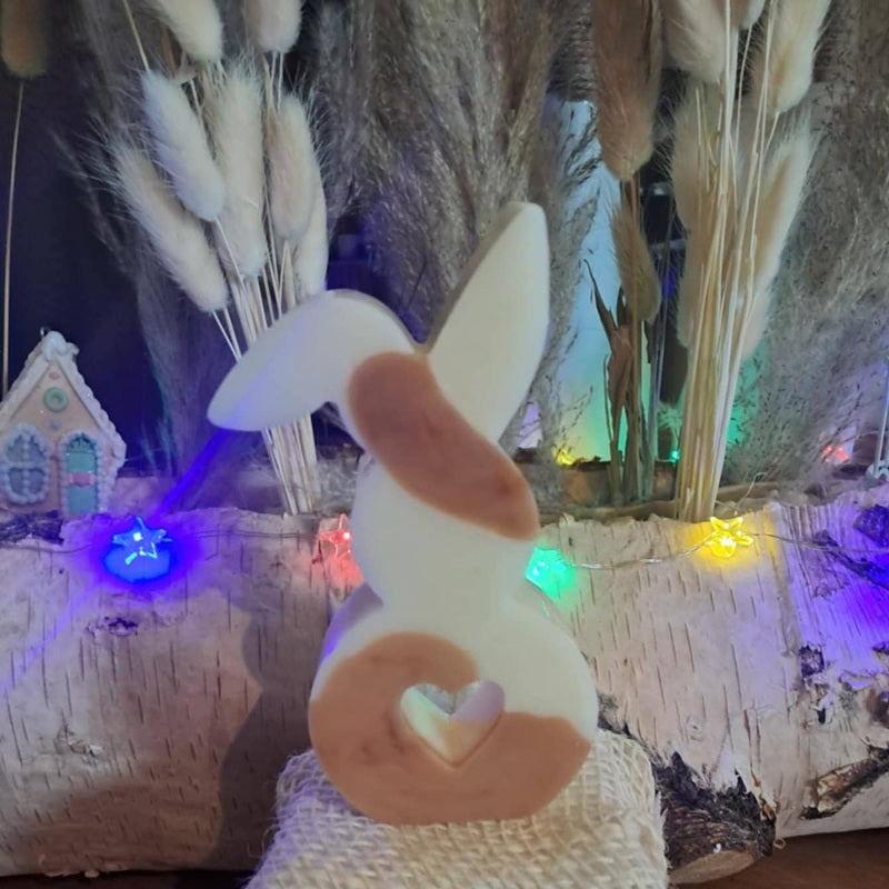Bougie artisanale représentant un petit lapin bicolore avec un cœur sculpté, disponible en format pot de 265g ou palet de 80g, décoration de chambre et cadeau de naissance.