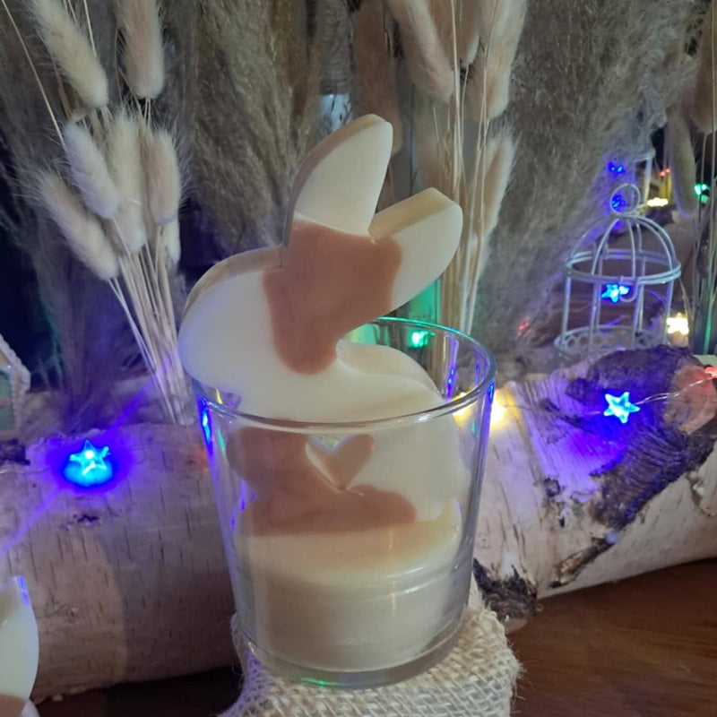 Bougie artisanale représentant un petit lapin bicolore avec un cœur sculpté, disponible en format pot de 265g ou palet de 80g, décoration de chambre et cadeau de naissance.