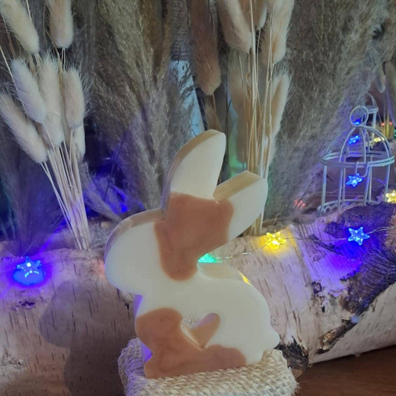 Bougie artisanale représentant un petit lapin bicolore avec un cœur sculpté, disponible en format pot de 265g ou palet de 80g, décoration de chambre et cadeau de naissance.