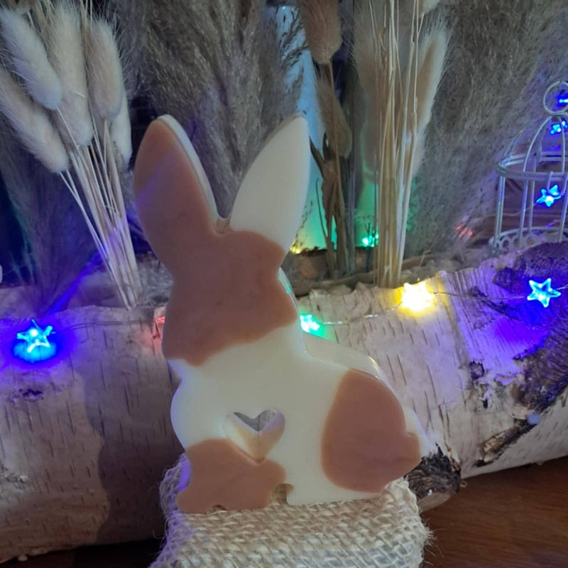 Bougie artisanale représentant un petit lapin bicolore avec un cœur sculpté, disponible en format pot de 265g ou palet de 80g, décoration de chambre et cadeau de naissance.