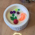 Bougie artisanale de 200g dans un pot blanc texturé, décorée de fondants en cire en forme de fruits (fraises, baies), design coloré et gourmand.