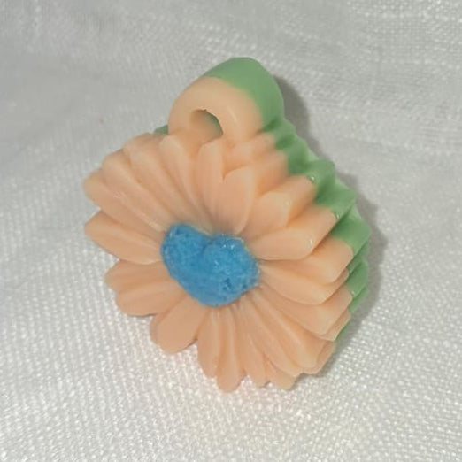 Bougie artisanale en forme de marguerite avec pétales blancs détaillés et cœur bleu contrastant, posée sur une étagère de décoration style cottagecore.