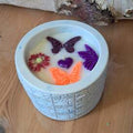 Bougie artisanale de 200g dans un pot blanc texturé, décorée de fondants en forme de papillons, fleurs et cœurs colorés, design printanier et poétique.