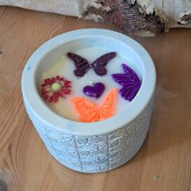 Bougie artisanale de 200g dans un pot blanc texturé, décorée de fondants en forme de papillons, fleurs et cœurs colorés, design printanier et poétique.