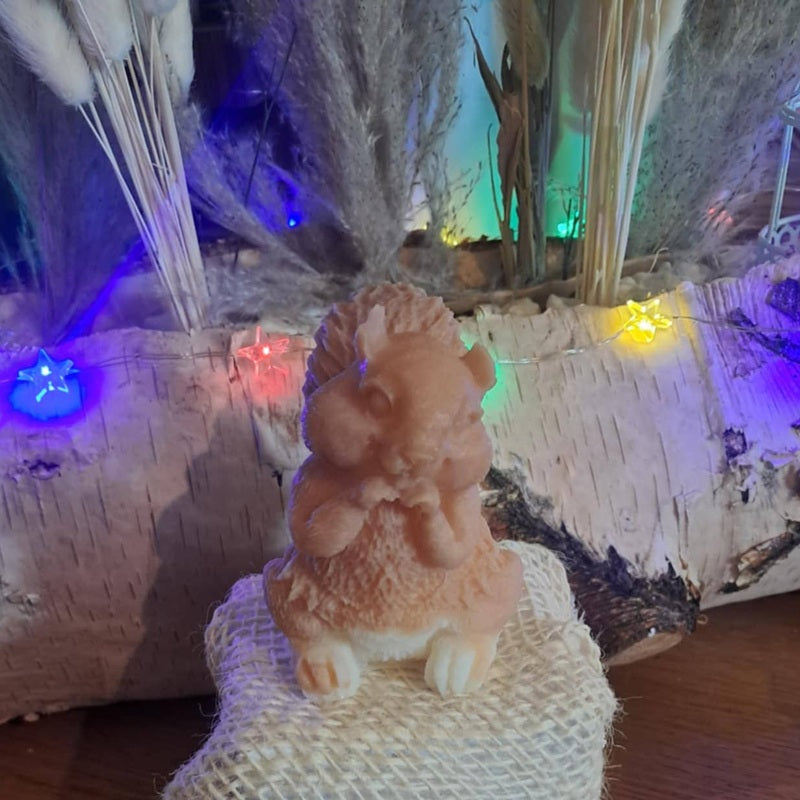 Bougie artisanale bicolore représentant un écureuil tenant une noisette, disponible en format pot en verre 265g ou figurine sculptée 80g.