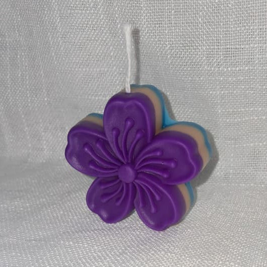Petite bougie artisanale en forme de fleur de cerisier (Sakura) avec un dégradé de bleu, violet et crème, idéale pour une décoration de table zen.