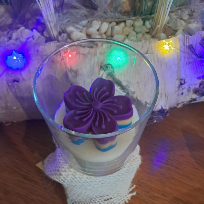 Bougie artisanale en forme de fleur de cerisier avec dégradé de couleurs violet, bleu et crème, dans son pot.
