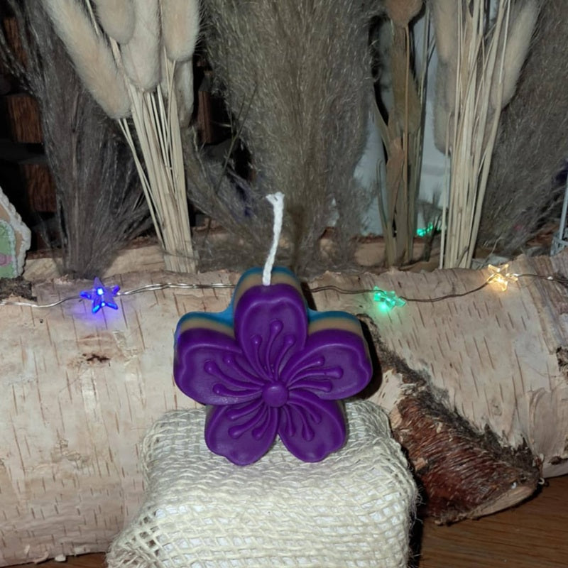 Bougie artisanale en forme de fleur de cerisier avec dégradé de couleurs violet, bleu et crème.