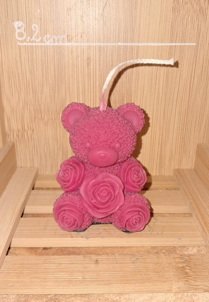 Bougie artisanale en forme d'ourson avec un nœud papillon sculpté et des motifs de roses sur les pattes, disponible en plusieurs couleurs pour la Saint-Valentin.