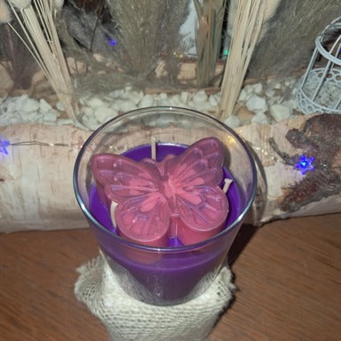 Bougie artisanale en verre avec un papillon rose sculpté sur le dessus, nommée L'Éveil d'Elya, symbole de renouveau et d'espoir.