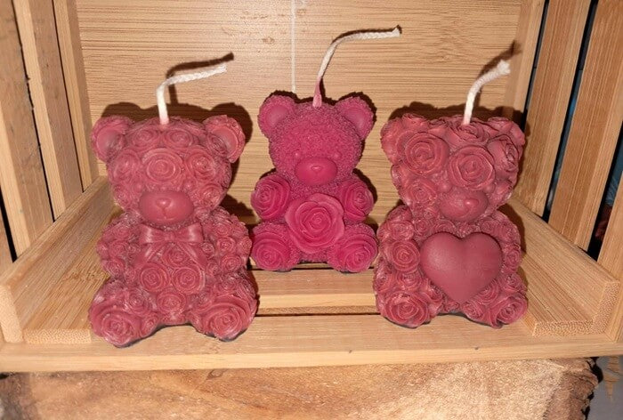 Ensemble de trois bougies oursons artisanales : l'un avec un nœud papillon, l'un avec un cœur et l'autre sculpté de roses, présentés pour la Saint-Valentin.