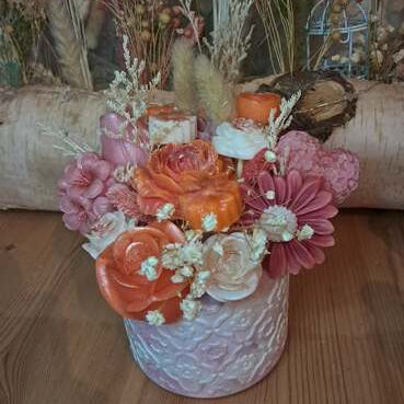 Composition florale artisanale printanière dans un pot en plâtre résine travaillé, contenant un ourson de roses et des fleurs en cire parfumée, utilisables comme fondants de cire.