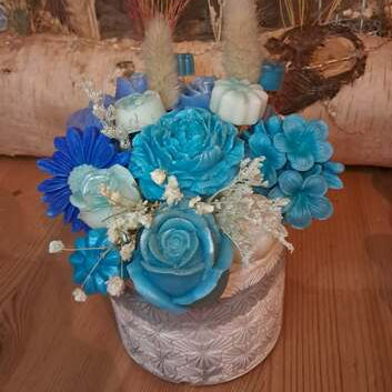 Composition florale artisanale bleue dans un pot en plâtre résine travaillé, contenant un ourson de roses et des fleurs en cire parfumée, utilisables comme fondants de cire.