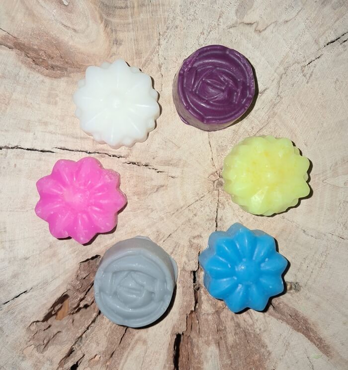Assortiment de petits fondants parfumés artisanaux en forme de fleurs et de roses multicolores, fabriqués en cire végétale biodégradable.